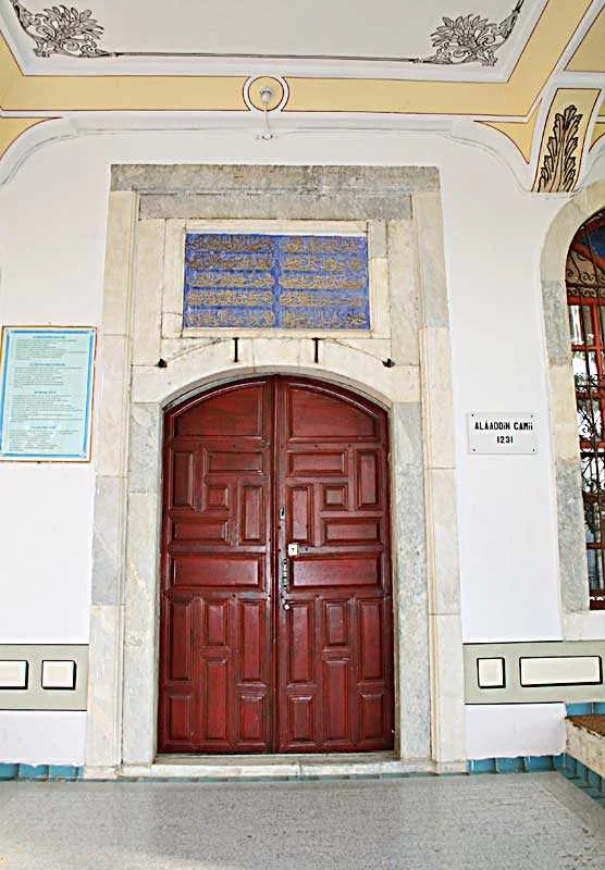 Koyu kahverengi ahşap kapı, mavi çiniler ve Arap harfleriyle süslü
