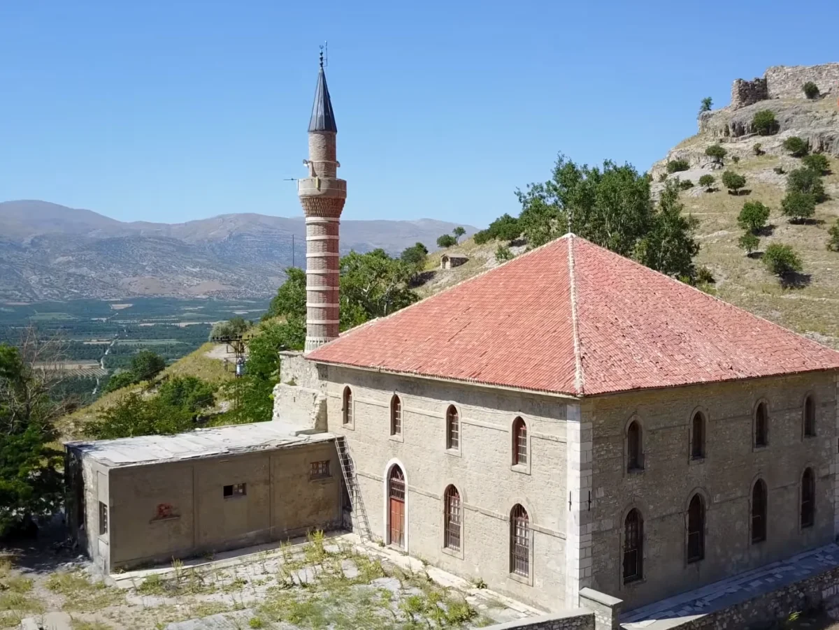 Alaaddin Camii, taş duvarları ve tuğla minaresi ile doğal manzarada yer alıyor.