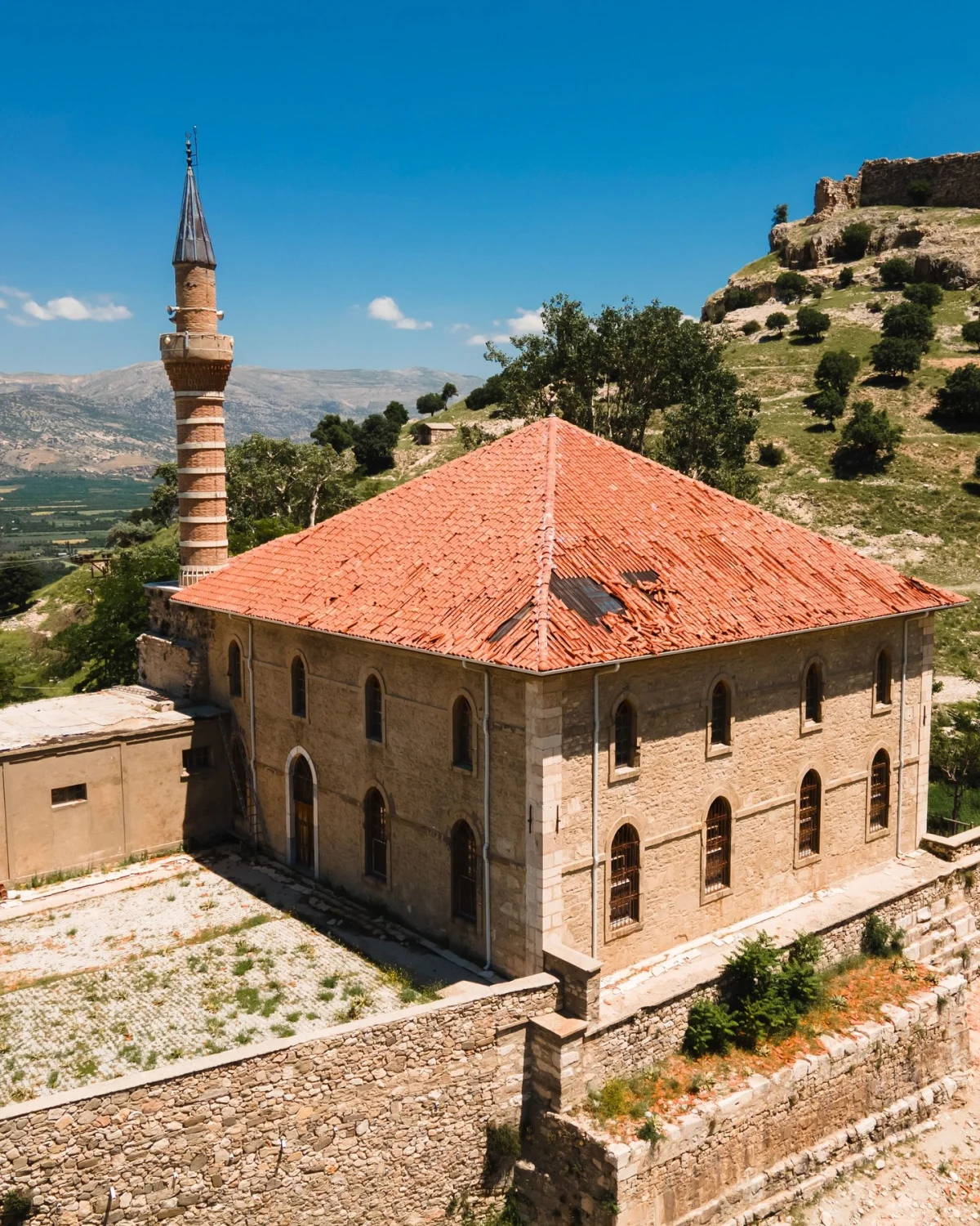 Taş yapılı Alaaddin Camii, kırmızı kiremit çatısı ve minaresiyle tarihi bir görüntü sunuyor.