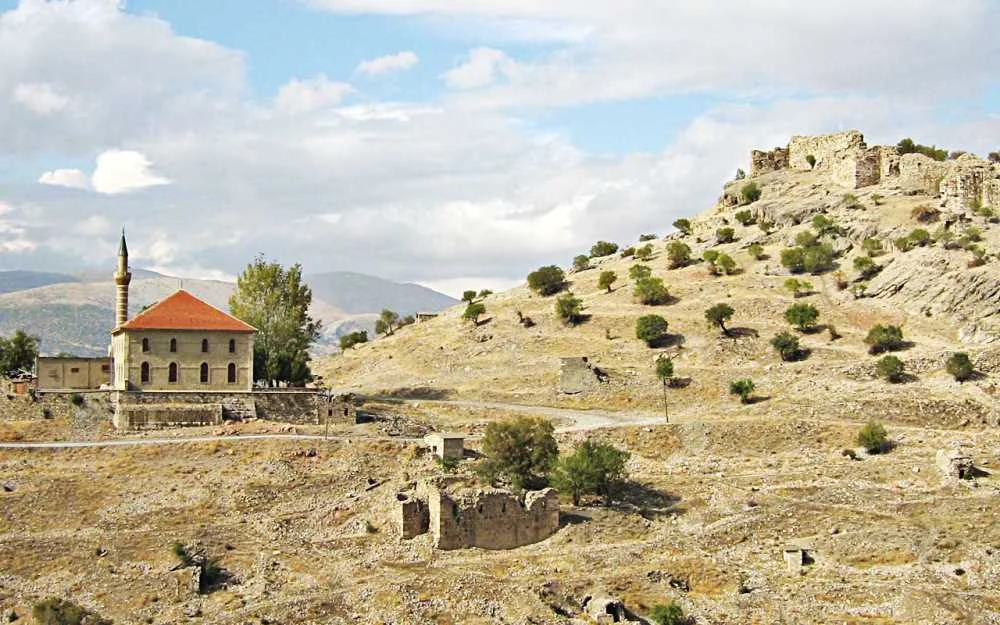 Kurak arazide yer alan Alaaddin Camii ve minaresi, arka planda harabe kalıntılarıyla birlikte görülüyor.