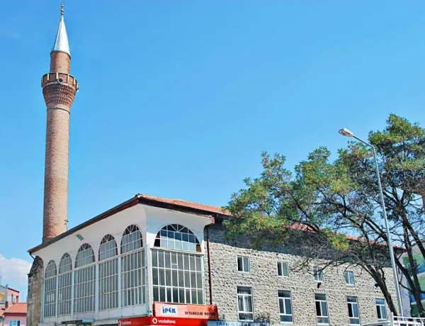 Alaca Mescit Camii'nin minaresi, avlulu yapısı ve arka plandaki yeşil ağaçlar.