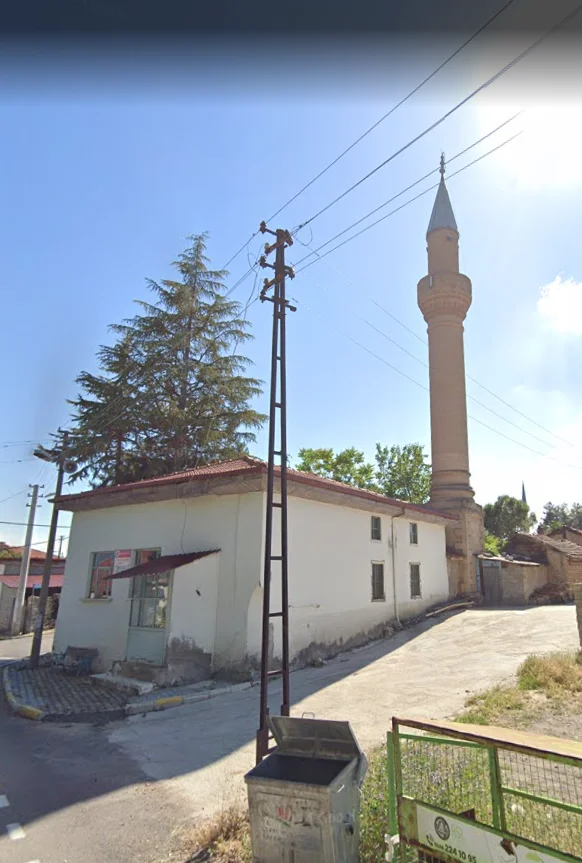 Alaca Mescit Camii'nin silindirik minaresi ve arka planda yeşil ağaçlar.