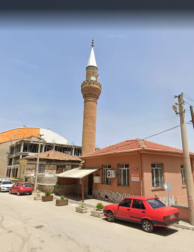 Ali Efendi Camii'nin minaresi, etrafındaki binalar ve parke taşlı yol üzerinde kırmızı bir araba.