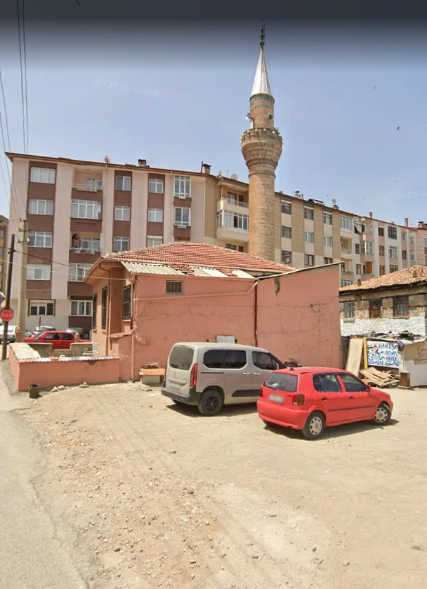 Gri ve kırmızı araçların önünde, minaresi yükselen Ali Efendi Camii ve modern apartmanlar