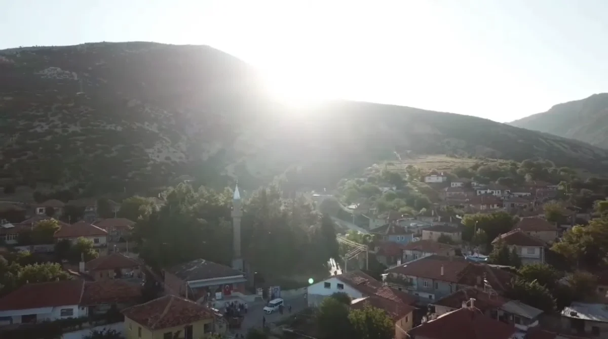 Köydeki cami kulesi, dağlar ve yöresel evler ile çevrili bir manzara