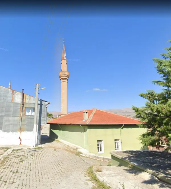 Yeşil bir bina önünde taş döşeli yol ve yüksek minare manzarası