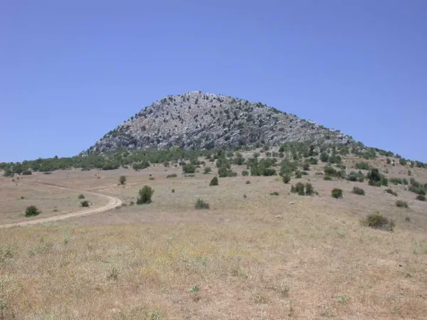 Açık gökyüzü altında kayalık tepe, sarımsı alan ve kıvrılan patika