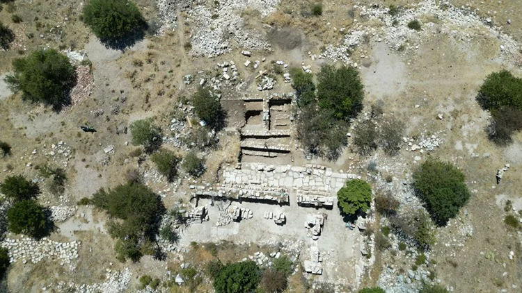 Yukarıdan çekilmiş Timbriada antik kenti arkeolojik alanı, taş kalıntıları ve yeşil bitki örtüsü ile dolu.