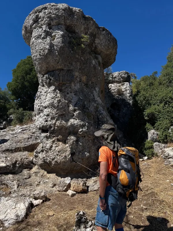Büyük doğal taş oluşumuna bakan kişi, sırt çantasıyla selfie çekiyor.