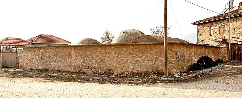 Taşlardan yapılmış, yuvarlak çatılı tarihi bir binanın dış cephesi ve çevresindeki ağaçlar
