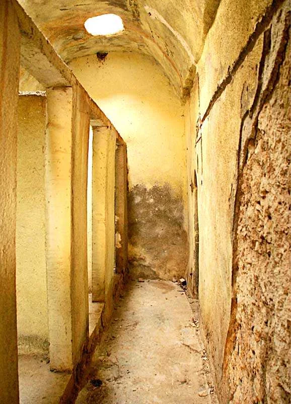 Dar, taş kaplama geçit; sarı duvarlar ve kemerli tavan gözlemleniyor.