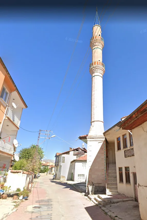 Zarif mimariye sahip cami minaresi, arka planda tarihi evler ve yeşil ağaçlar