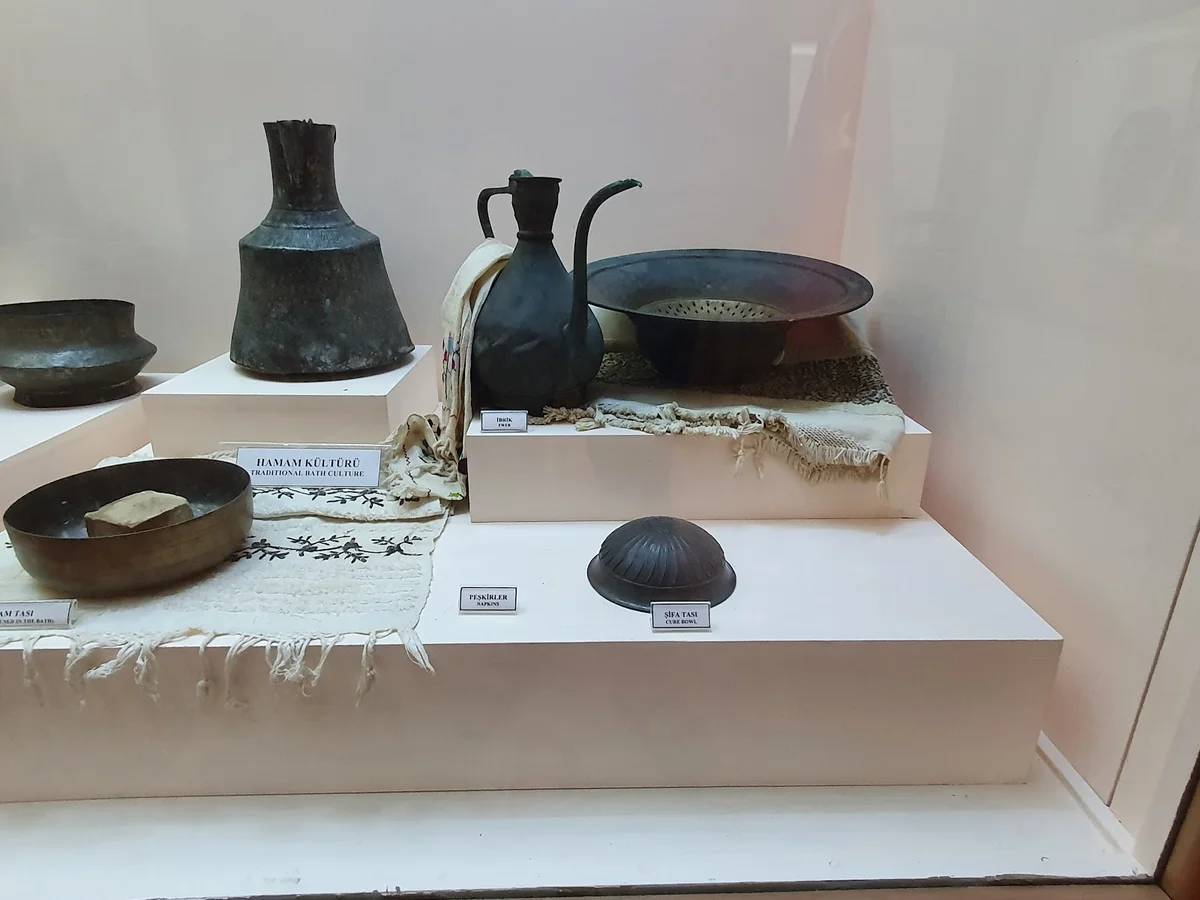 Çeşitli metal kaplar, sürahi ve tabakların sergilendiği geleneksel el sanatı eserleri.