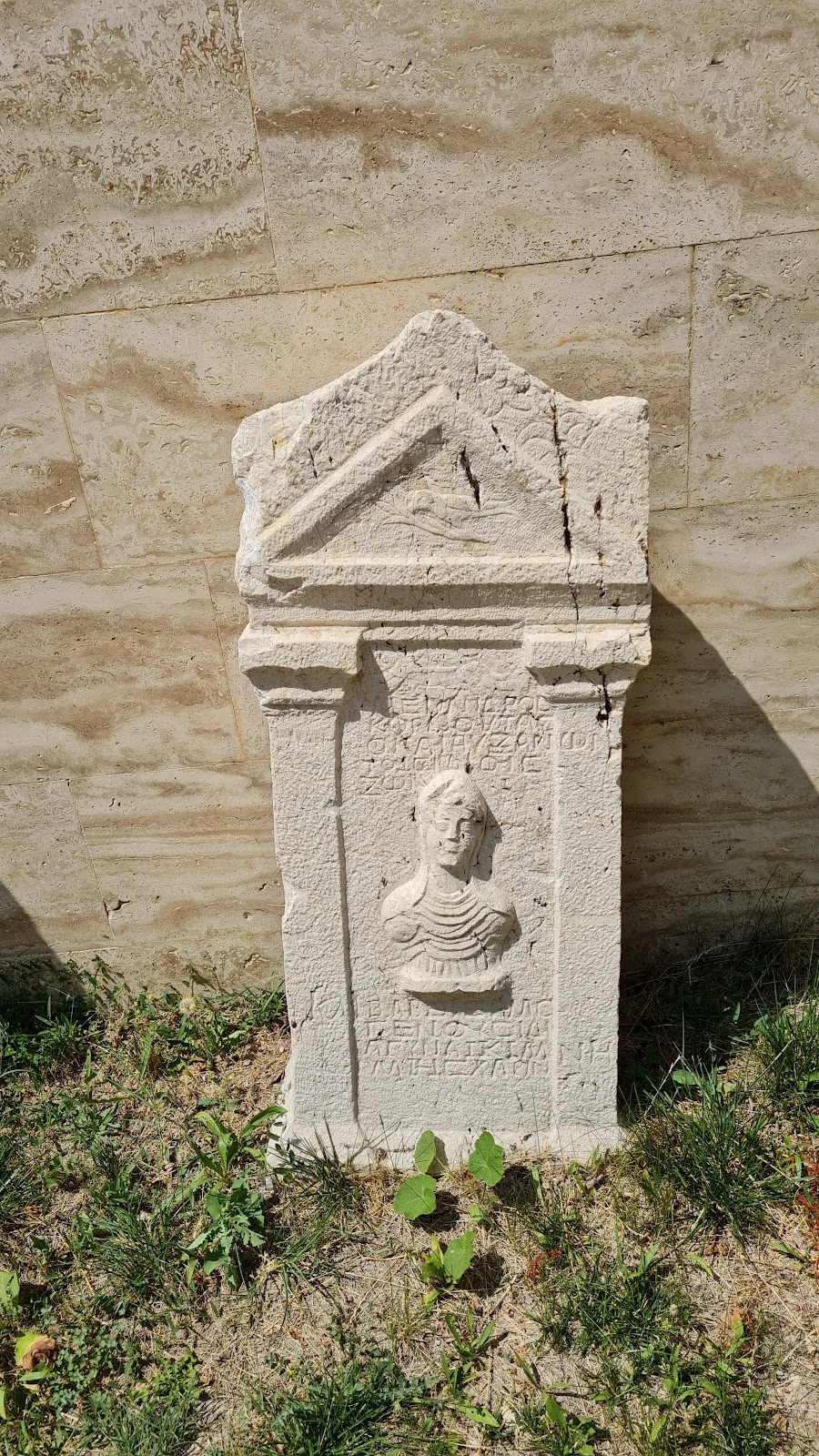 Tarihi mezar taşı, insan figürü ve doğal zemin ile çevrili.