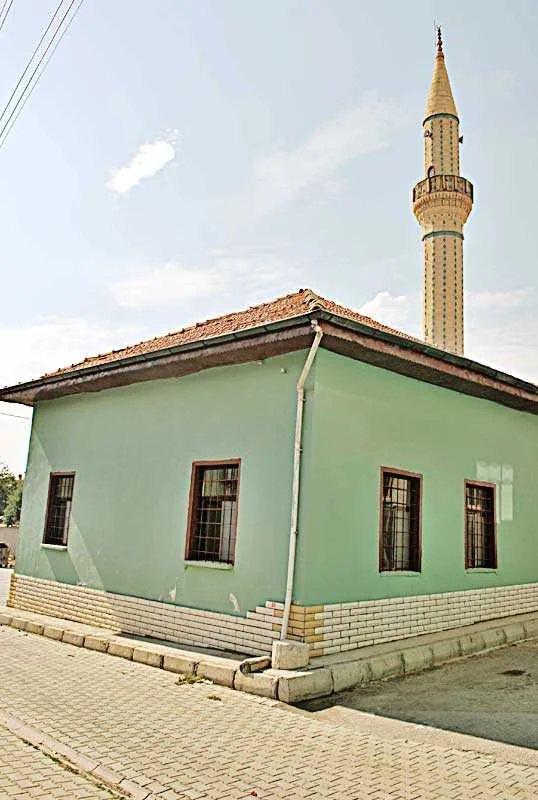 Kaşaşağı Camii'nin minaresi ve yeşil duvarlı binası açık havada görünmekte.