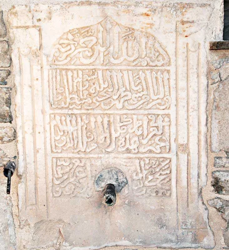 Taş yüzeyde Arapça yazılarla süslü tarihi çeşme duvarı
