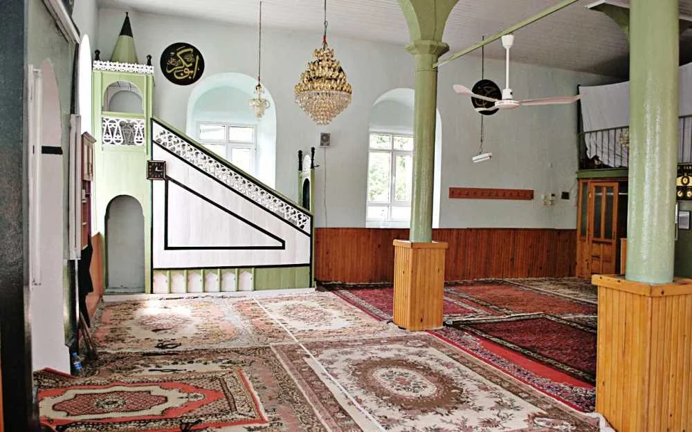 Ferah bir cami iç mekanında yeşil-beyaz minber ve desenli halılar
