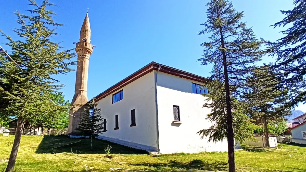 Tarihi Yılanlıoğlu Camii, uzun minaresi ve yeşil ağaçlarla çevrili huzur dolu bir manzarada