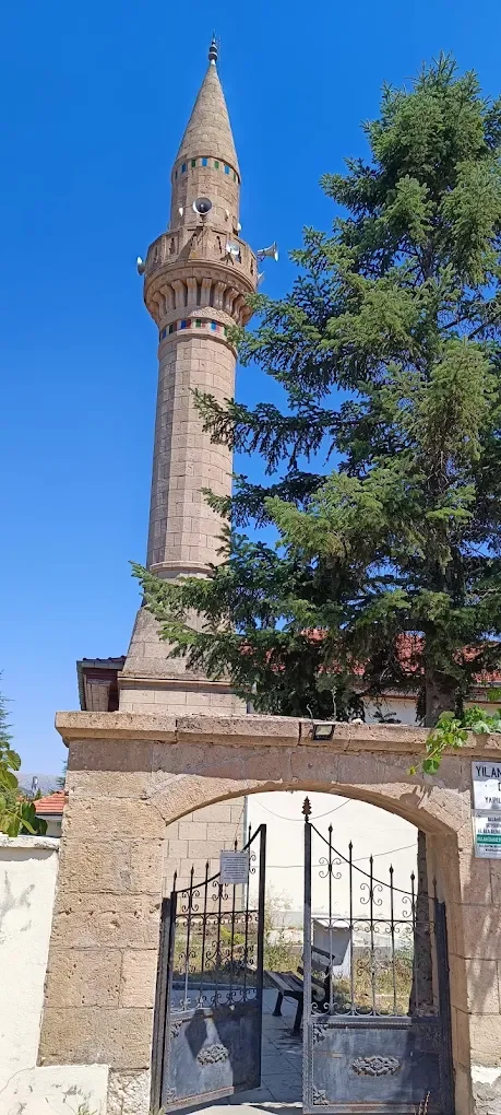 Mavi gökyüzü altında yükselen Yılanlıoğlu Camii'nin minaresi ve bahçe kapısı.