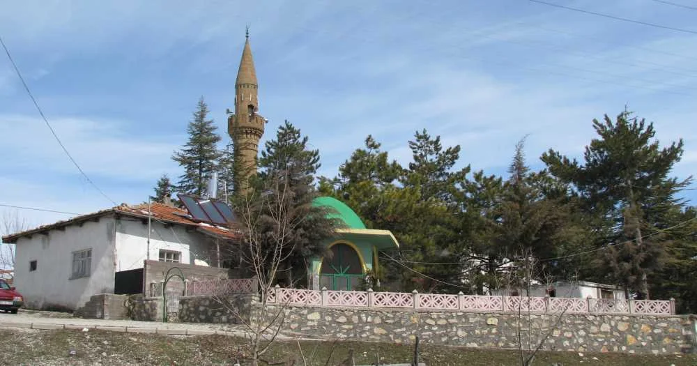 Yeşil çatılı Yılanlıoğlu Camii ve yanında sade bir ev, doğal bir manzara içinde.