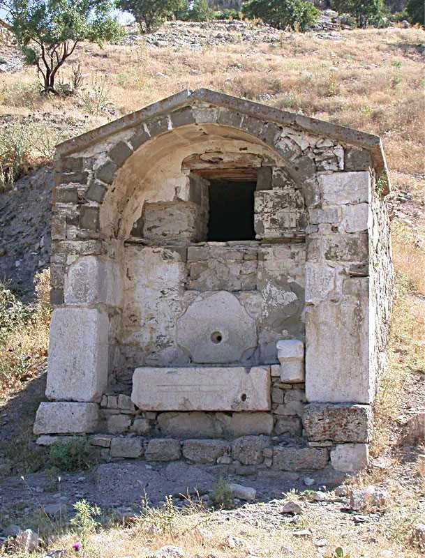 Gafle Çeşmesi: Tarihî Mirasın Taş Kemerleri - Kurumuş Otlar ve Tarih! Taş bir çeşme, kemerli çatısı ve etrafındaki kurumuş otlar ile dikkat çekiyor.