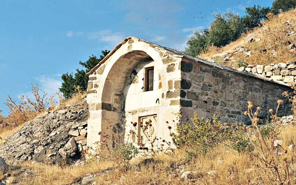 Tarihi bir mimari eser - taşlardan yapılmış kavisli çatı, sarımsı otlar ve ağaçlar! Taşlardan yapılmış kavisli çatıya sahip eski bir çeşme, etrafında sarımsı otlar ve yeşil ağaçlar yer alıyor.