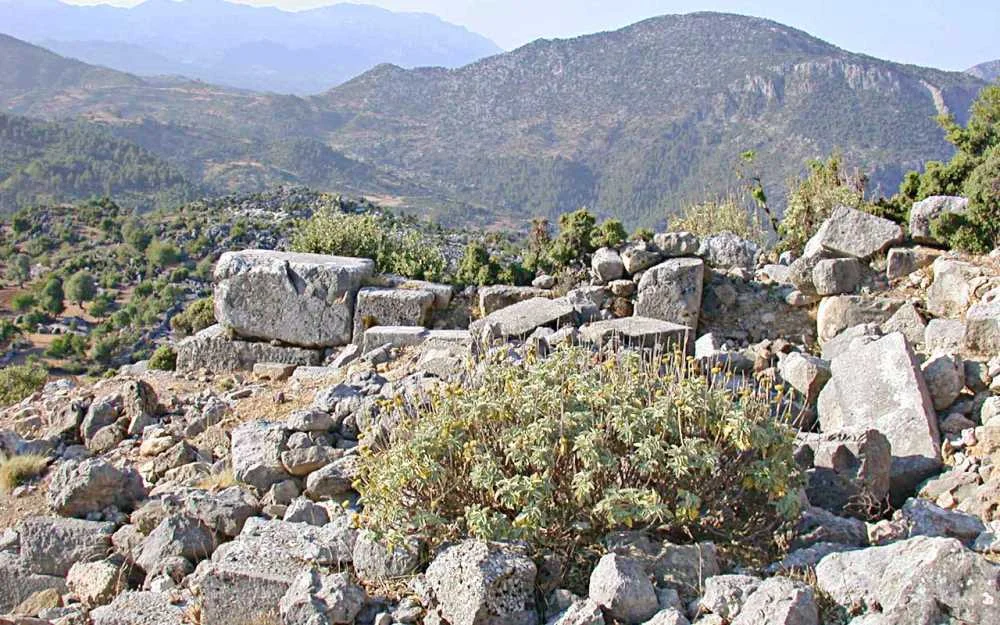 Doğal dağlık alanda taş kalıntıları ve yeşil bitkilerle dolu bir manzara.