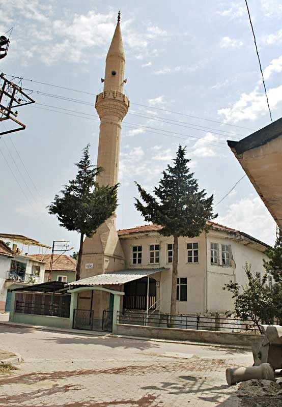 Beyaz duvarlı cami ve yüksek minaresi, açık mavi gökyüzü altında yer alıyor.