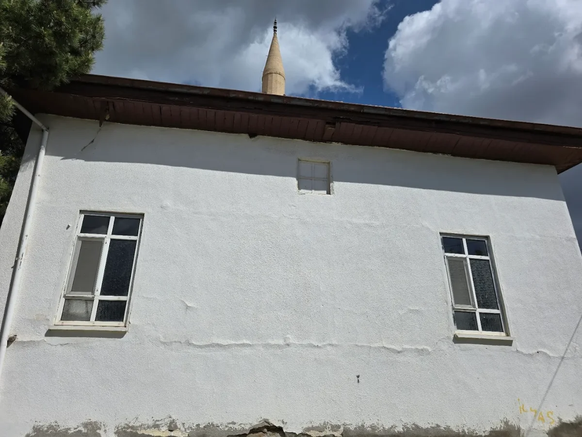 Beyaz dış cepheli cami, ahşap çatı ve minaresi ile bulutlu gökyüzü arka planda.