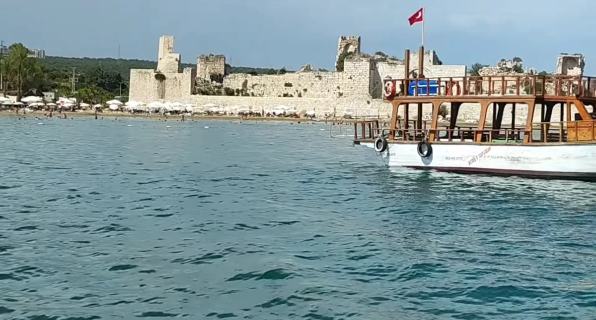 Deniz üzerinde Türk bayrağı dalgalanan tekne ve arka planda tarihi kalenin kalıntıları