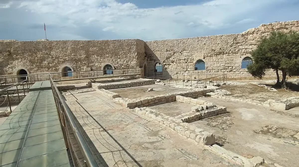 Taşlardan inşa edilmiş büyük bir kalıntı, yüksek duvarlar ve mavi gökyüzüyle çevrili.