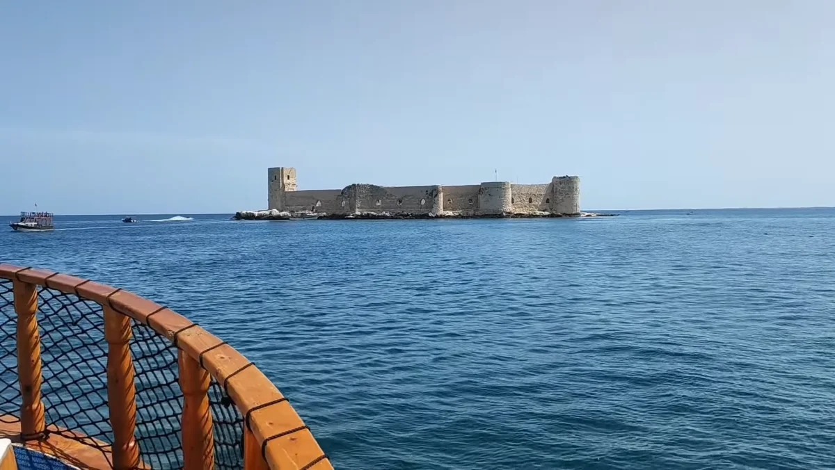 Mavi deniz ortasında tarihi Kız Kalesi, arka planda açık gökyüzü ve teknelerle birlikte
