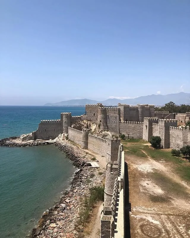 Mamure Kalesi - Tarihin İzleri ve Akdeniz Manzarası! Deniz kenarında büyük bir kale, sağlam taş duvarlar ve kuleler ile çevrili, arka planda mavi deniz ve dağlar