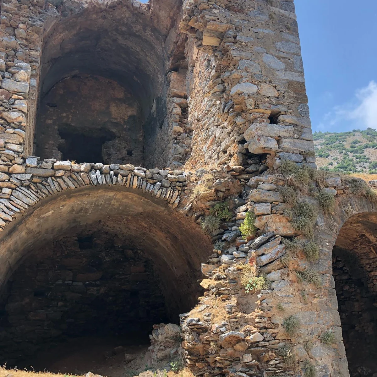 Yıkılmış taş yapılar ve doğa ile birleşen tarihi kalıntılar görünmektedir.