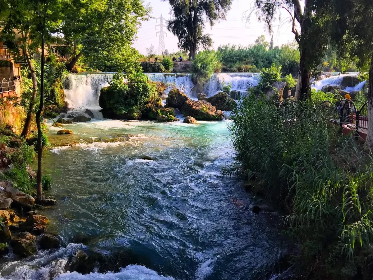 Tarsus Şelalesi'nin Huzur Verici Güzelliği - Yeşil ve Mavi Su Arasında Yeşil ağaçların arasında akan küçük bir şelale, açık mavi ve yeşil suyla kayalıkların arasından düşüyor.