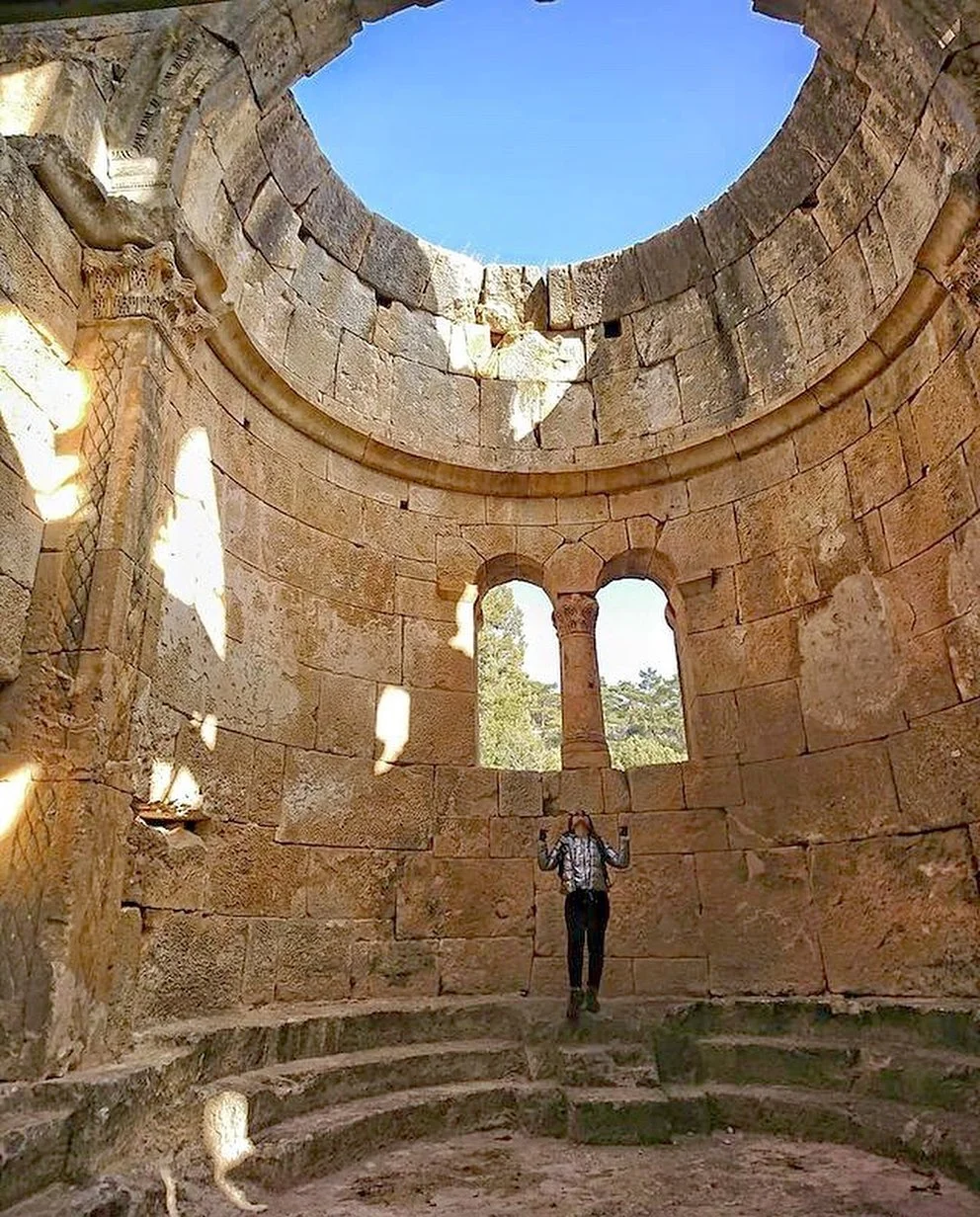 Alahan Manastırı'nın Tarihi ve Mimari Güzellikleri - İç mekanda taş bloklar ve sütunlar Alahan Manastırı'nın iç mekanında büyük taş bloklar ve oymalı sütunlar, bir kişiyle birlikte aydınlatılıyor.