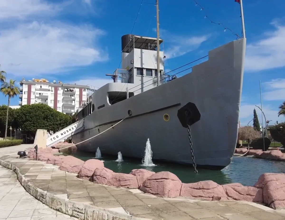TCG Nusret: Tarihin İhtişamı ve Doğanın Buluşması TCG Nusret mayın gemisi, çevresindeki yeşil bitkiler ve fıskiyelerle sergileniyor.
