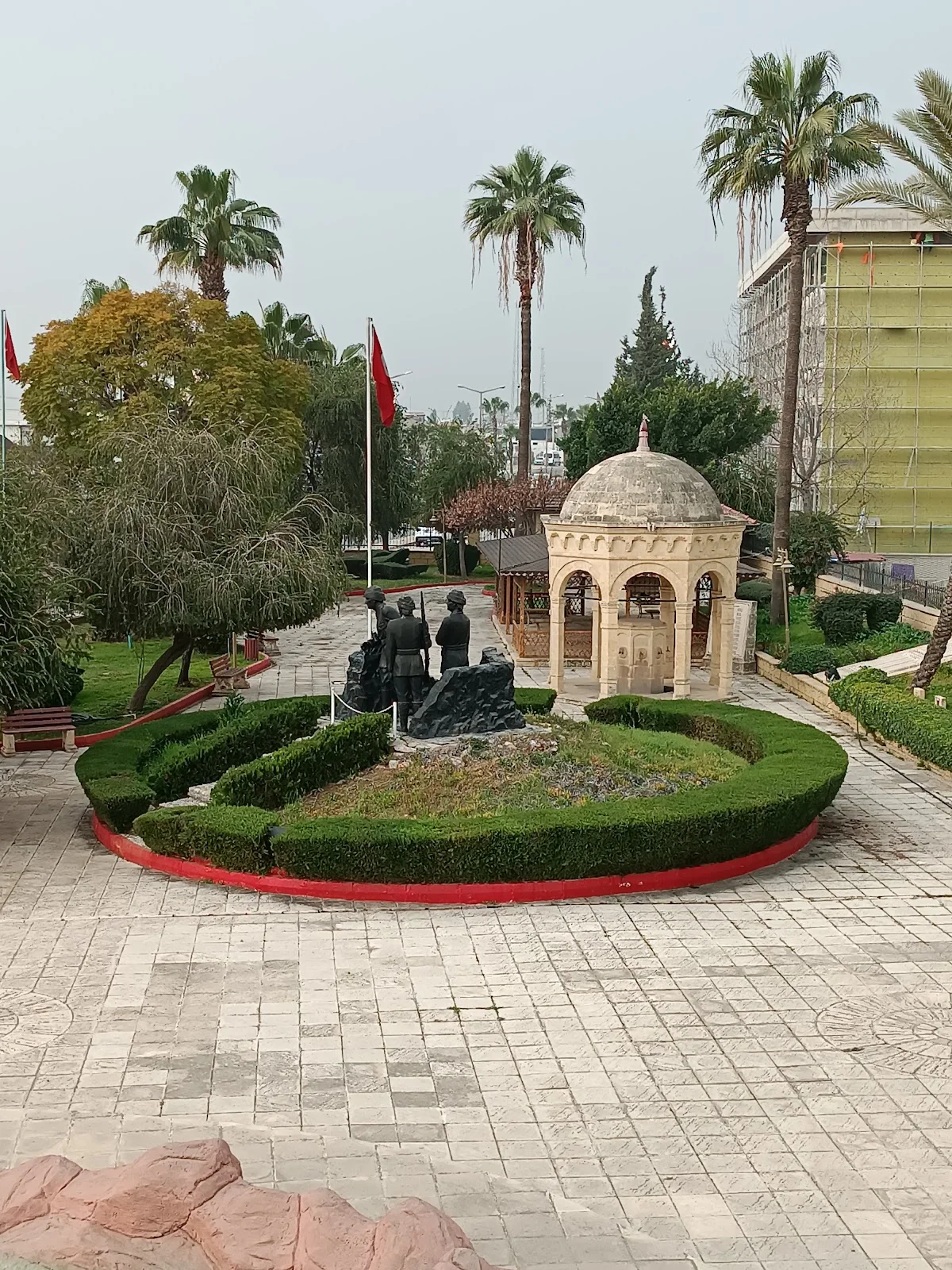 Nusrat Mayın Gemisi Parkı - Tarih ve Doğanın Kesişimi! Yeşil alan, heykel grubu, palmiye ağaçları ve Türk bayraklarıyla dolu park manzarası.