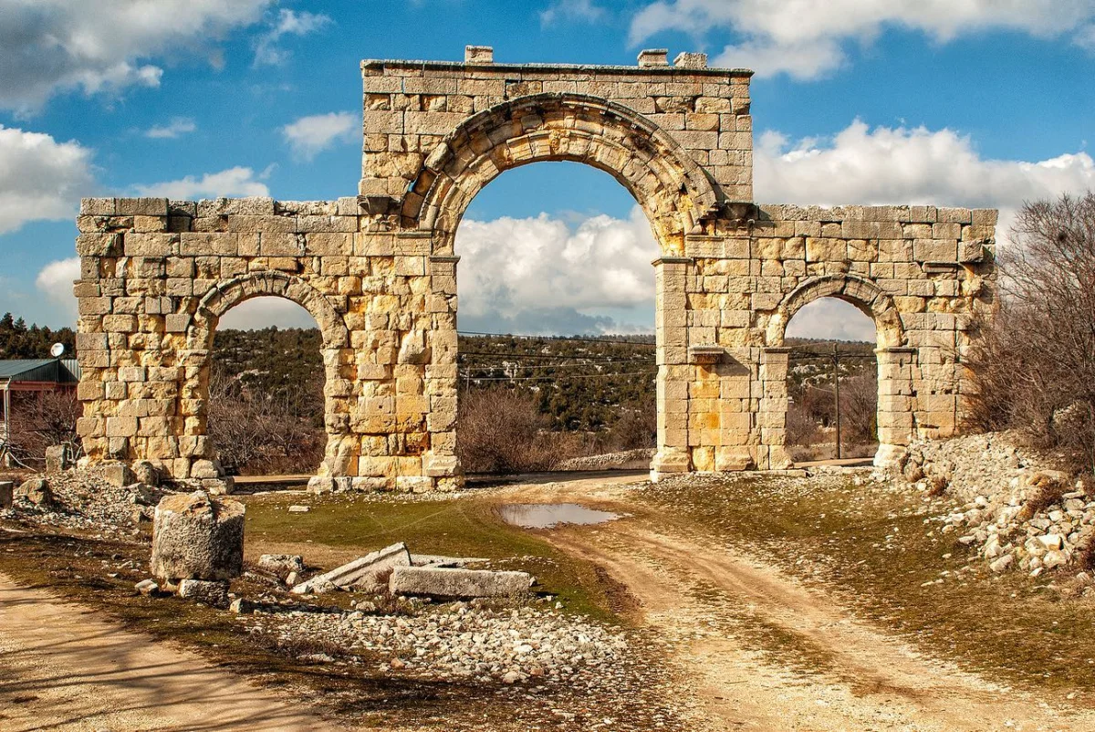 Antik Şehir Kapısı - Uzuncaburç'un Taş Yapısı ve Çevresi Uzuncaburç'ta büyük bir antik taş yapı, yuvarlak kemerli nişler ve doğal manzara ile çevrili.