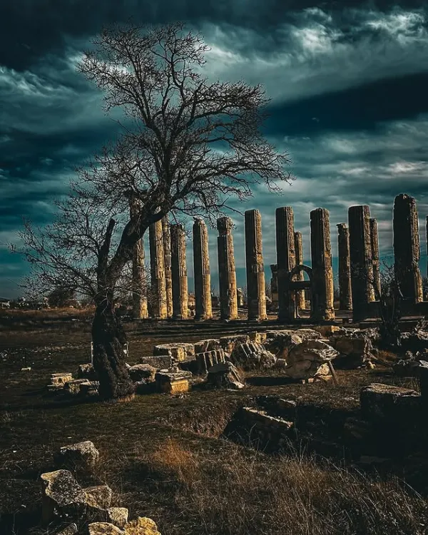 Silüetleri belirgin antik sütunlar karamsar bulutlar altında sıralanmış.