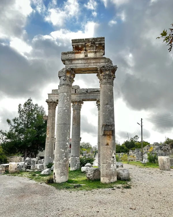 Detaylı işçilikle yapılmış sütunlar ve yeşil ağaçlarla çevrili antik kalıntılar