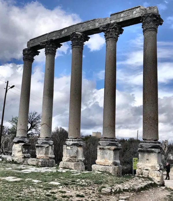 Antik sütun kalıntıları, bulutlu gökyüzü ve yeşil zemin ile doğal bir atmosfer oluşturuyor.