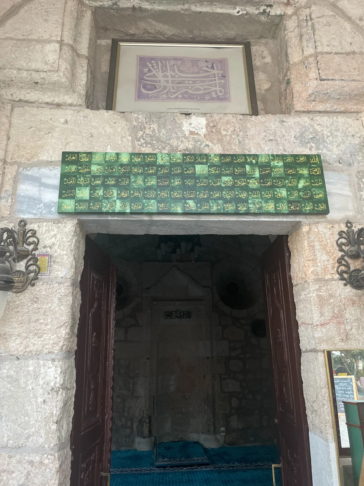 Girişin Görkemi - Bilal Habeşi Makamı ve Mescidi'nin Taş Duvarları! Eski taş duvar, yazılı sanat eseri ve ağır ahşap kapı ile dini bir mekan girişi.
