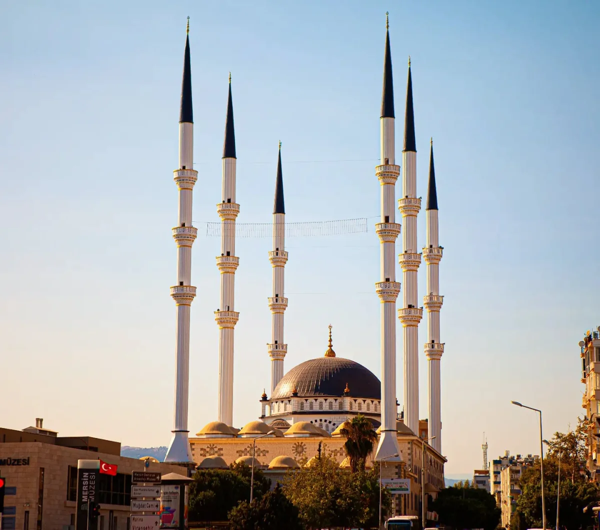 Muğdat Camii'nin Mimari Güzelliği - Minareler ve Kubbeler Yüksek altı minaresi ve geniş kubbesi ile Muğdat Camii, yeşil bitkilerle çevrili.