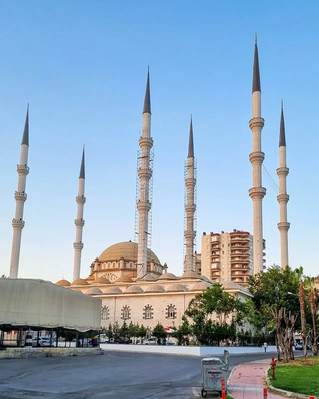 Muğdat Camii'nin Mimari ve Çevresi! Minareler ve Yeşil Alanlar Yüksek minarelere ve yuvarlak kubbeye sahip Muğdat Camii, yeşil alanla çevrili.