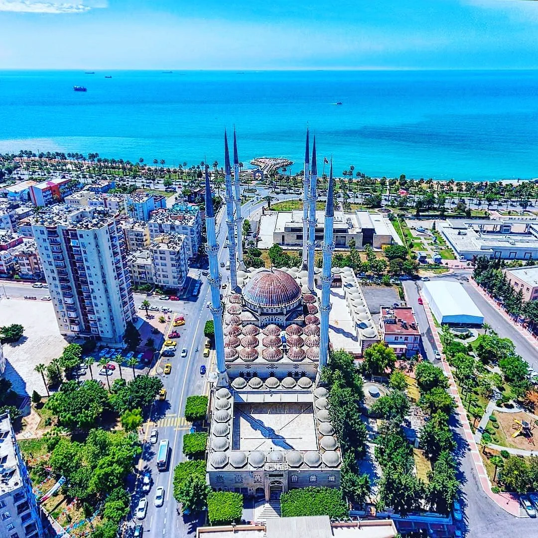 Tarihi ve Eşsiz Deniz Manzarası - Muğdat Camii'nin Sekiz Minaresi ve Çevresi Sekiz minaresi ve büyük kubbesiyle Muğdat Camii, yeşil ağaçlar ve berrak denizle çevrili.