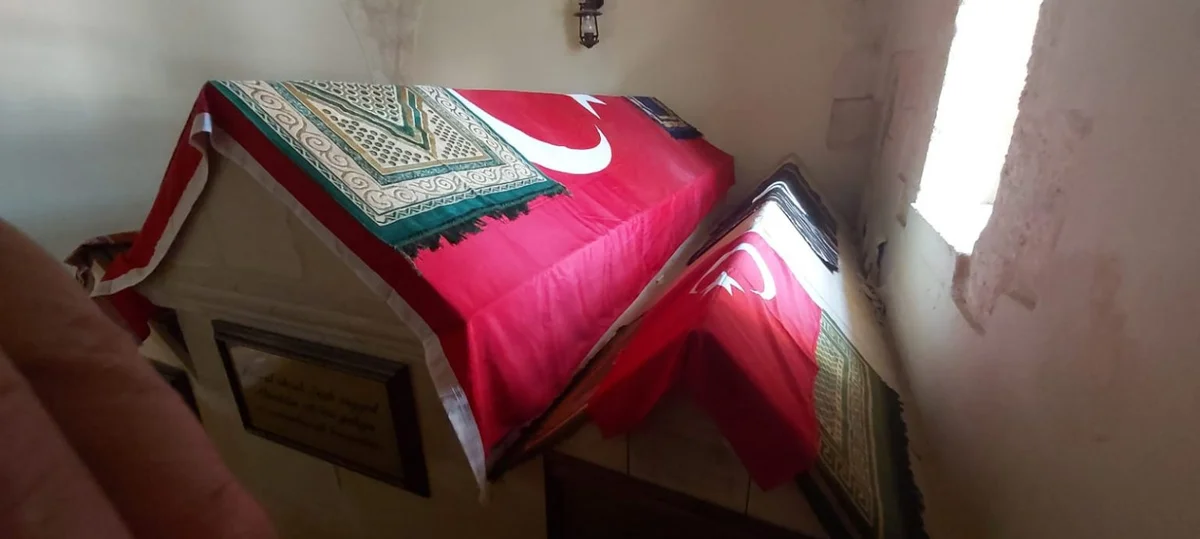 Zeyne Türbesi'nin İç Mekanı - Dini ve Kültürel Mirasın Sessiz Tanığı! Türk bayrağı ile örtülü mezar, geleneksel desenli örtü ve loş ışıkta bir iç mekan görüntüsü.