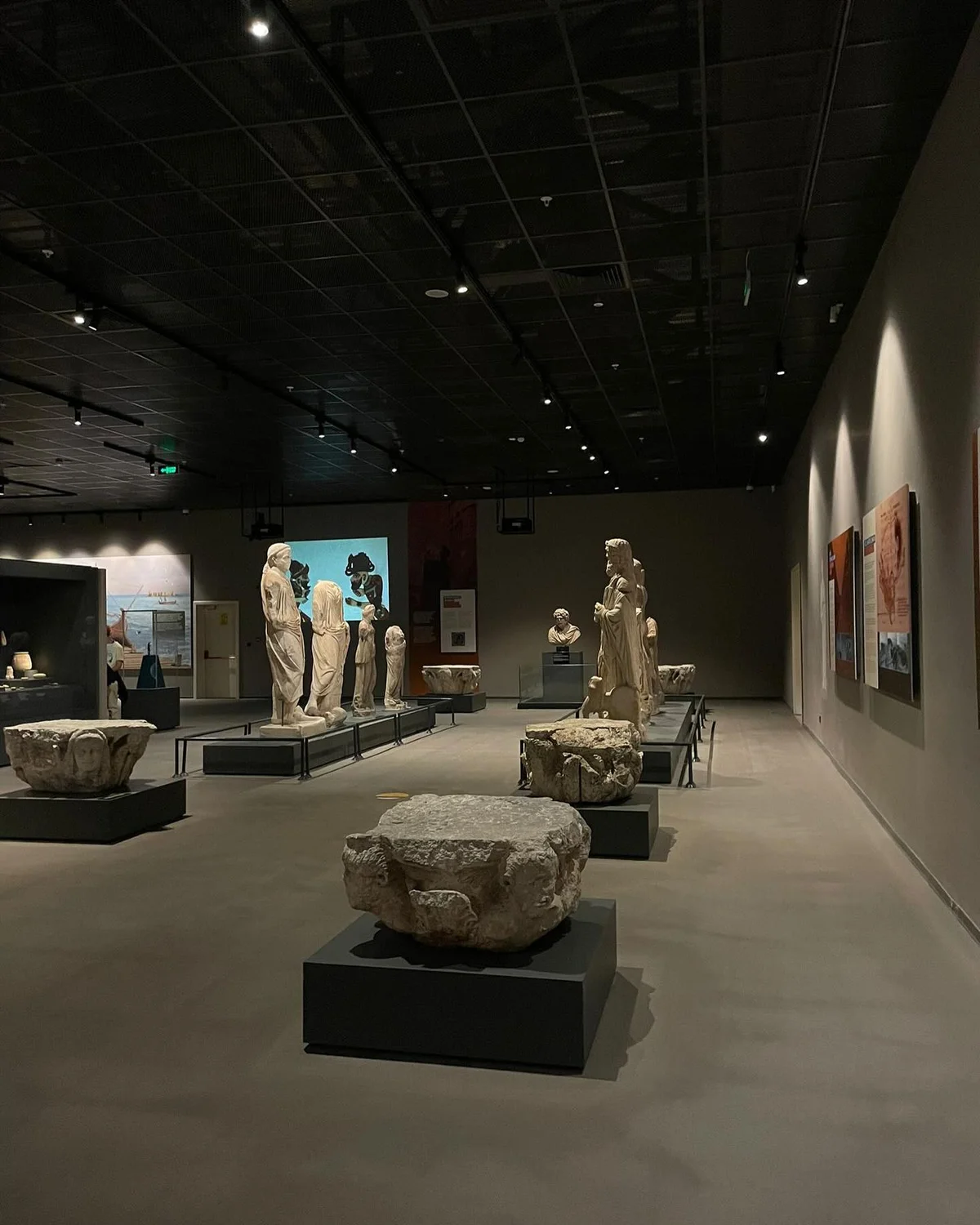 Modern Sergi - Loş aydınlatmada tarih ve sanat buluşması! Loş aydınlatma altında çeşitli taş heykeller ve tablolar sergileniyor.