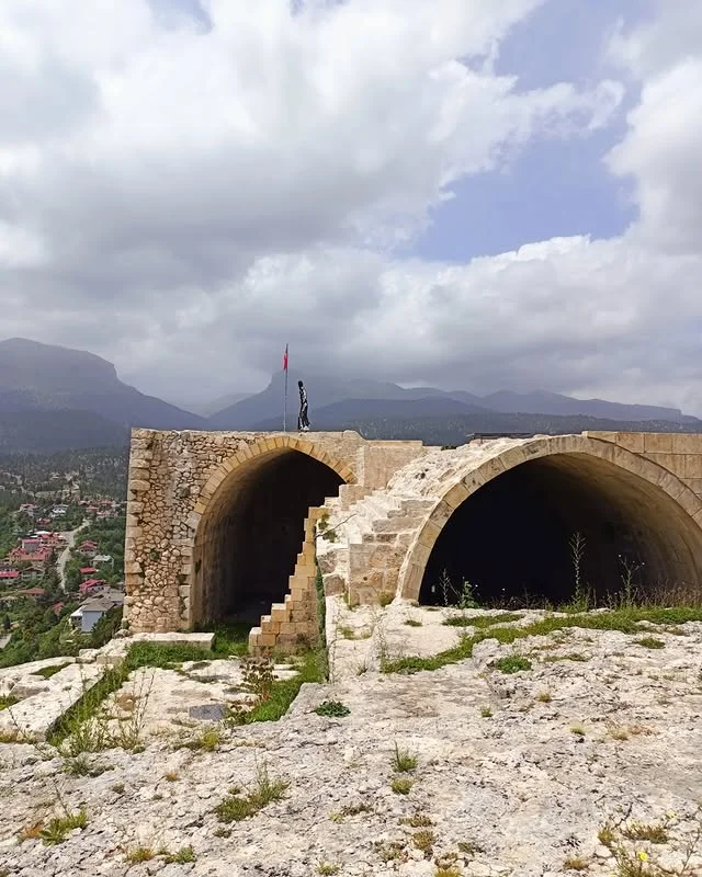 Namrun Kalesi: Tarihi Yapı & Doğal Güzellik - Dağlar ve Gökyüzü! Yükseltilmiş alanda tarihi Namrun Kalesi, dağlar ve bulutlu gökyüzü ile çevrili.