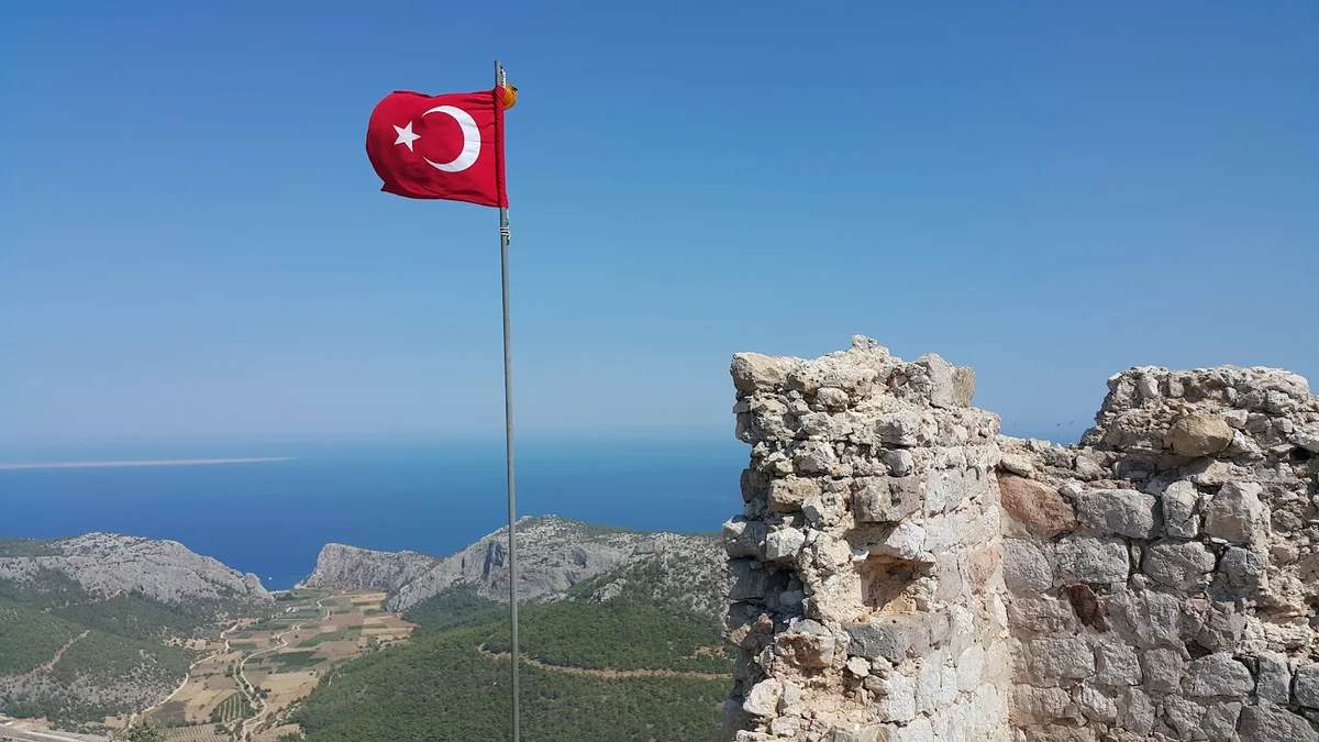 Silifke Kalesi: Tarih ve Doğa İç İçe - Bayraklar dalgalanıyor, tarih konuşuyor! Silifke Kalesi kalıntıları, dalgalanan Türk bayrağı ve mavi deniz manzarası.